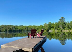 A wooden dock extending into a calm lake with two red Adirondack chairs on it. - Peaceful Cottage Retreat ~ 4 Season - Fantastic View (Dunchurch)