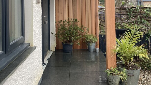Eine überdachte Veranda mit Holzbalken, einem Blumentopf und einer Tür.