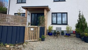 Ein zweistöckiges Haus mit einer Veranda, einem Holztor und einer Schotterzufahrt.