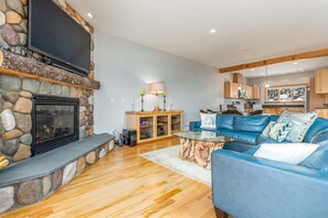 A living room with a stone fireplace, a television mounted on the wall, a blue sofa, and a wooden cabinet with a lamp.