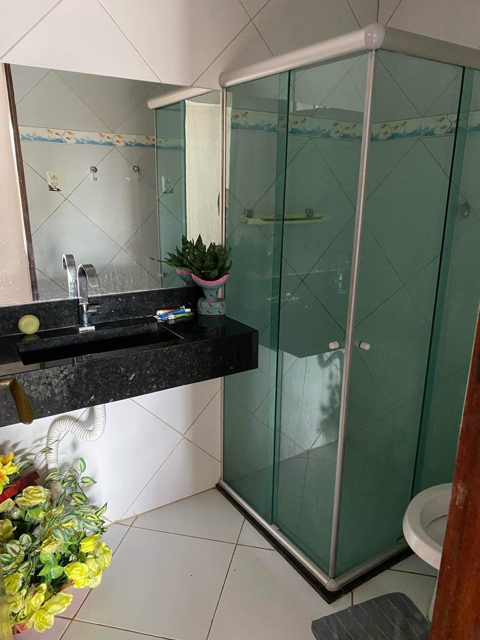 Un baño con cabina de ducha de vidrio, un lavabo con encimera negra y un espejo sobre el lavabo.