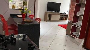 Een moderne keuken met een gasfornuis, een eethoek met rode stoelen, een televisie en een roodgekleurd tapijt.