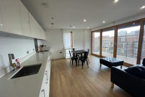 A modern kitchen with a dining area, large windows, and a black leather sofa.