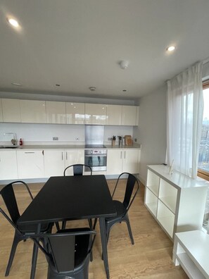 A modern kitchen with white cabinets, a black dining table, and a view of the city through large windows.