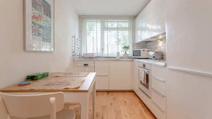 Una cocina moderna con armarios blancos, encimera de madera y una ventana con persianas.