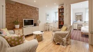 Una sala de estar moderna con pared de ladrillo, un televisor de pantalla plana, una estantería y un rincón de descanso acogedor con una silla y un sofá.