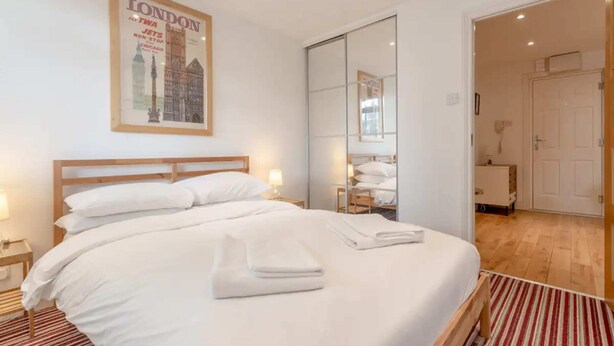 Habitación de hotel con una cama grande, un armario, un espejo y un cartel con monumentos de Londres.