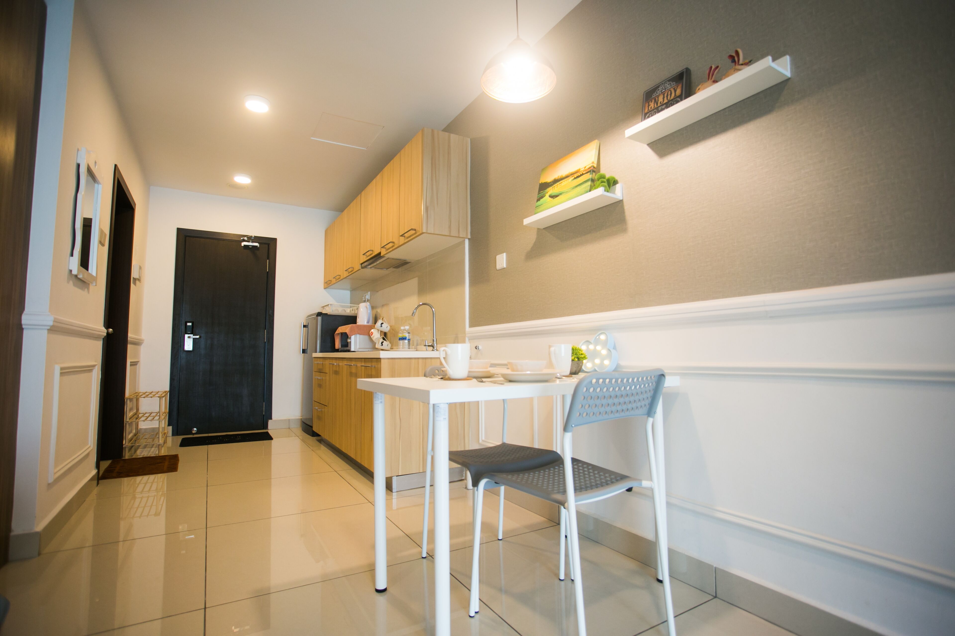 A modern kitchen with white cabinets, a white table, and a chair. There is a black door and a shelf with decorative items.