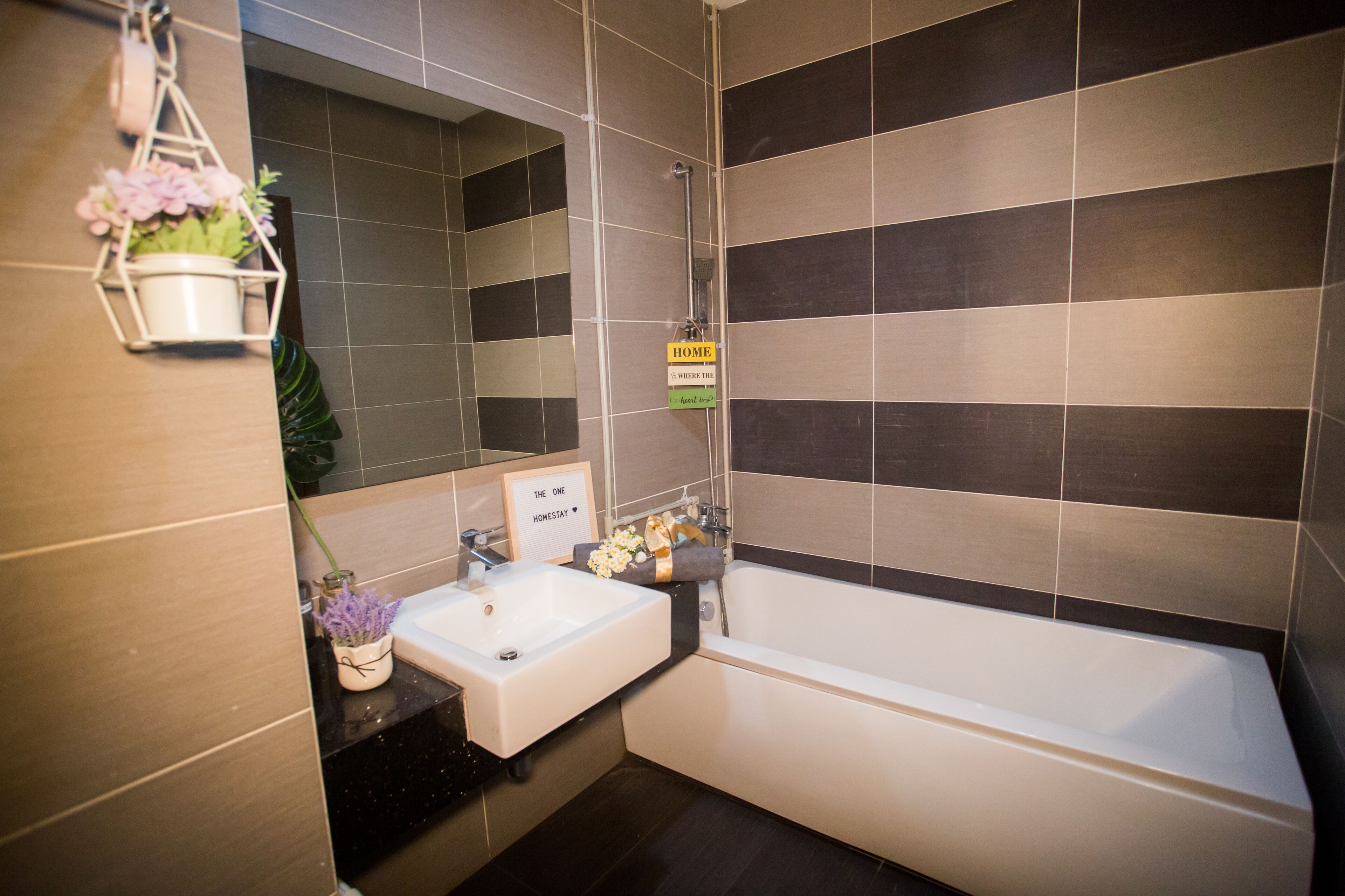 Un baño moderno con bañera, lavamanos y espejo. Hay un cartel que indica la ubicación y una planta pequeña en la encimera.