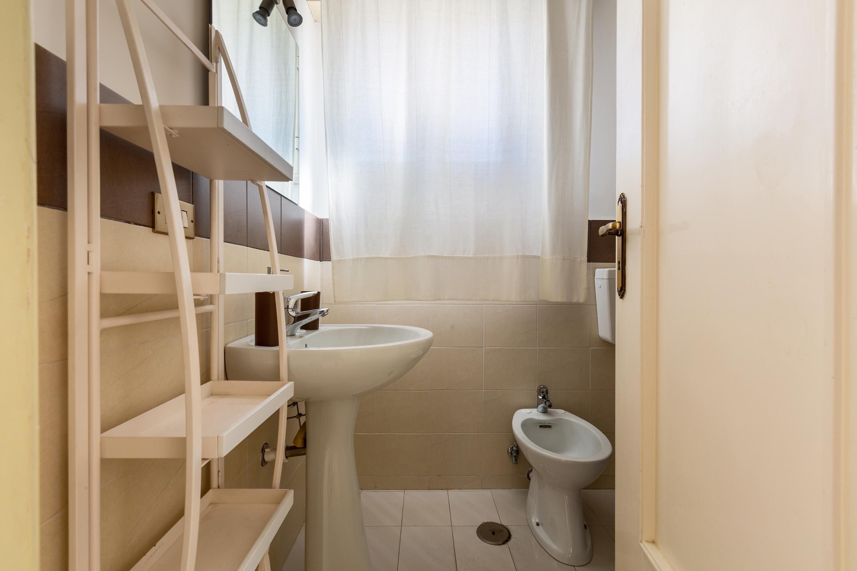 Ein kleines, sauberes Badezimmer mit Waschbecken, Bidet und Regalen.