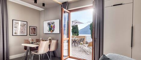 A modern living room with a sofa, a dining area with chairs and a table, and a balcony with outdoor seating.