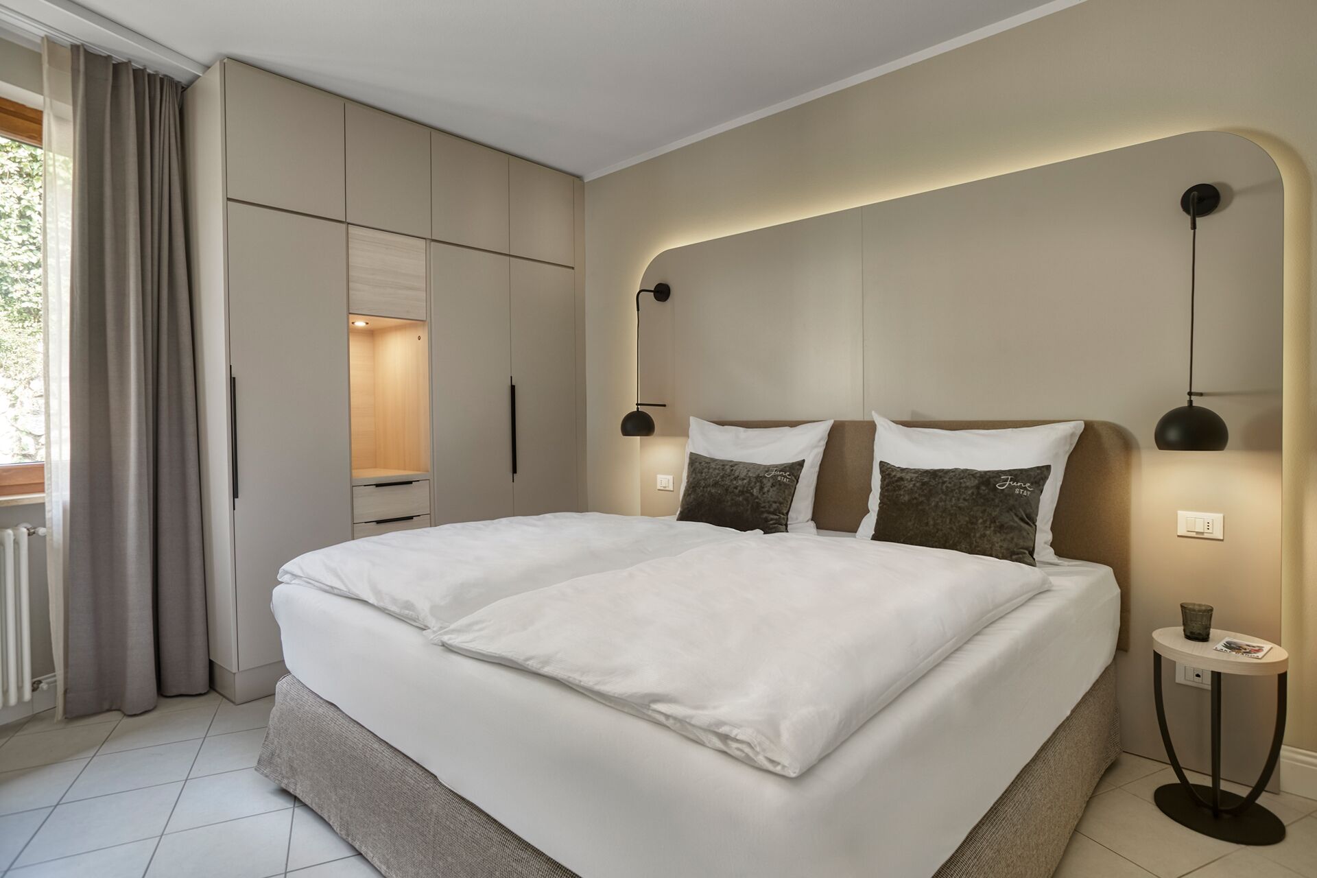 A modern bedroom with a large bed, built-in wardrobe, and bedside lamps.