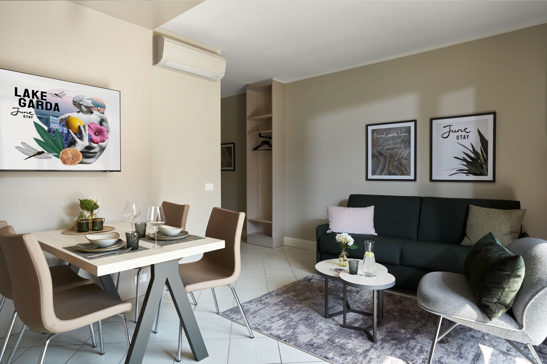 A modern living room with a dining area, a sofa, and a small table. There are framed pictures on the wall and a ceiling-mounted air conditioner.
