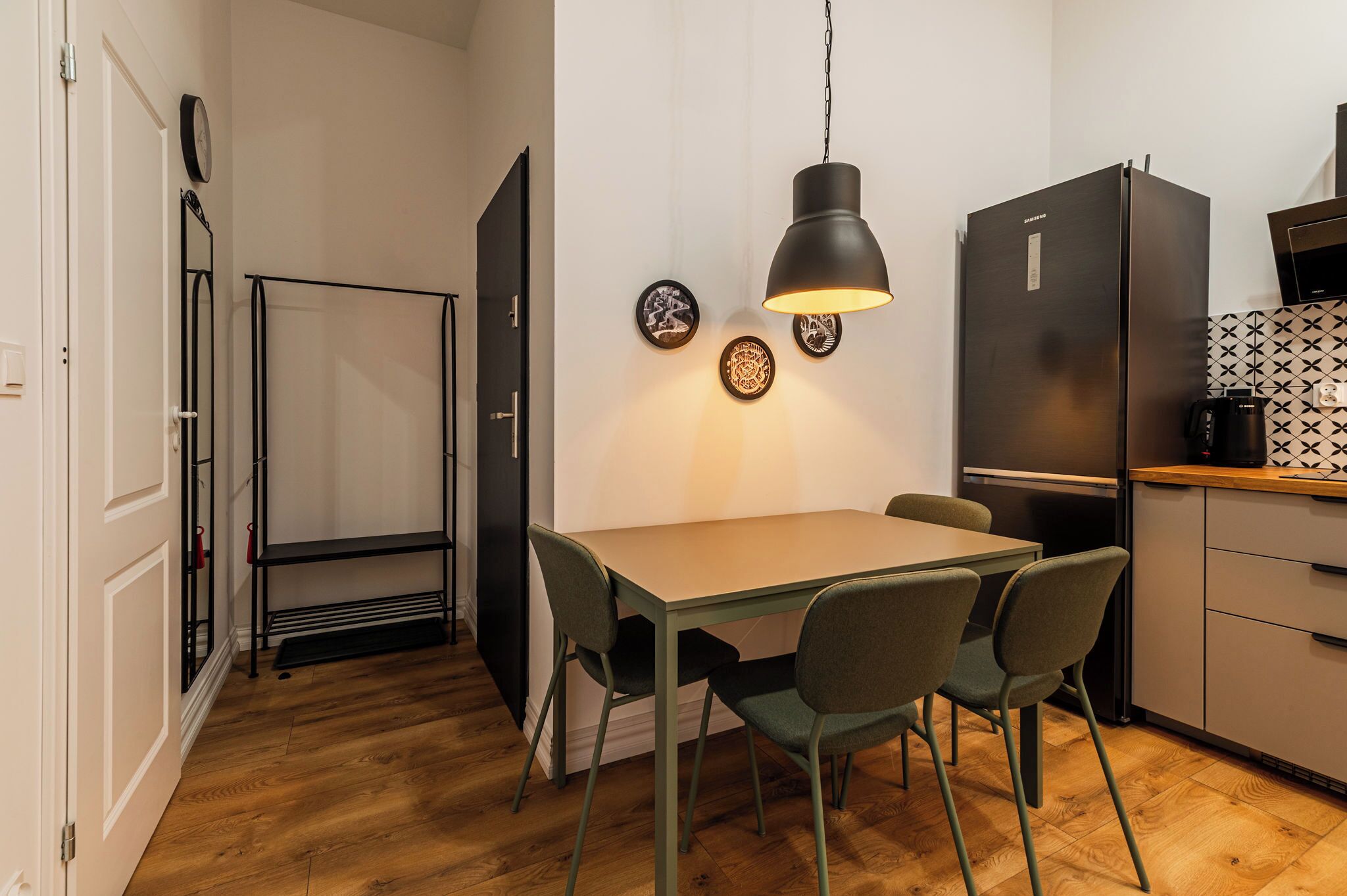 A compact kitchen with a dining table, chairs, a black refrigerator, and a hanging pendant light.