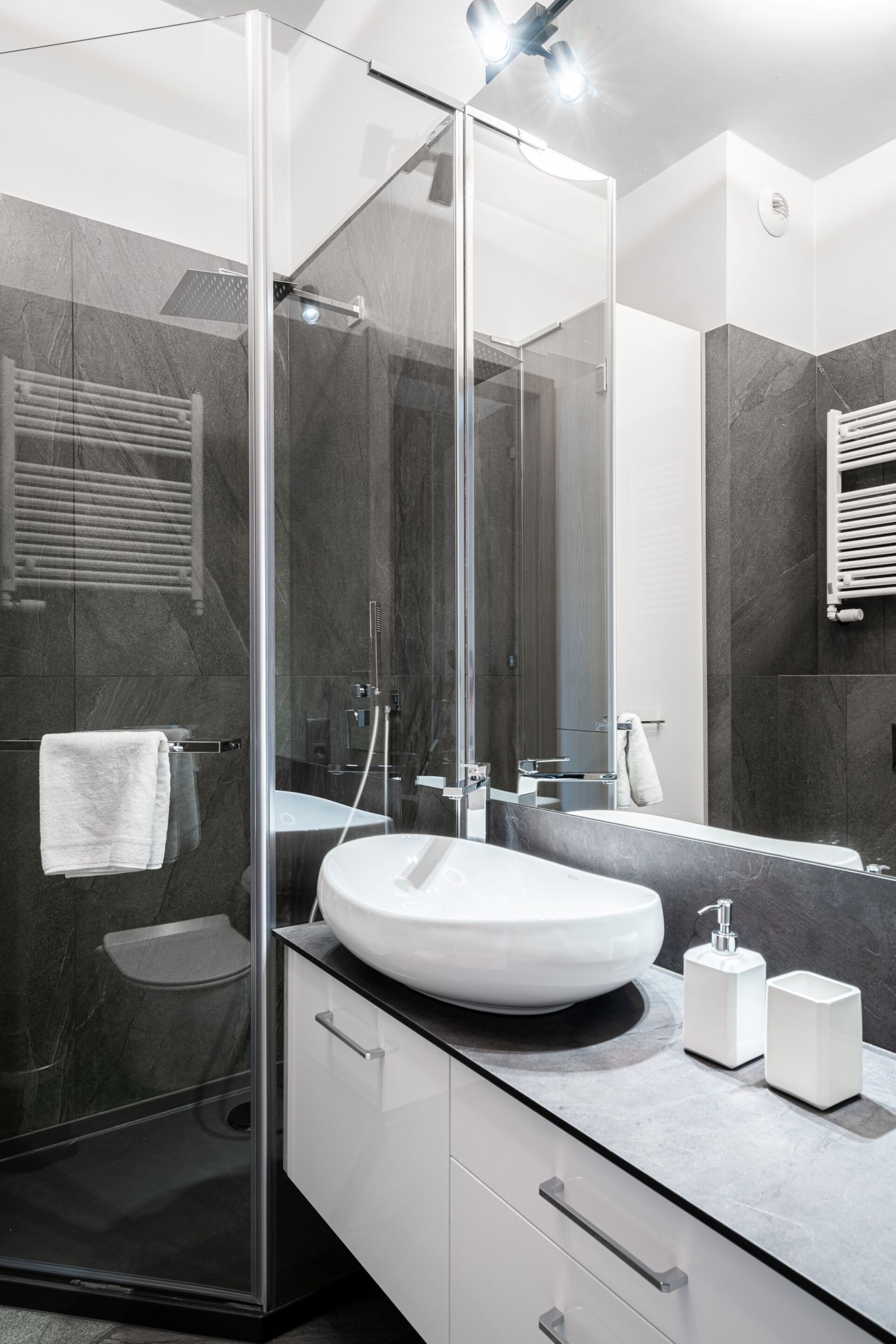 Un baño moderno con ducha separada por vidrio, un lavamanos blanco y un espejo grande.