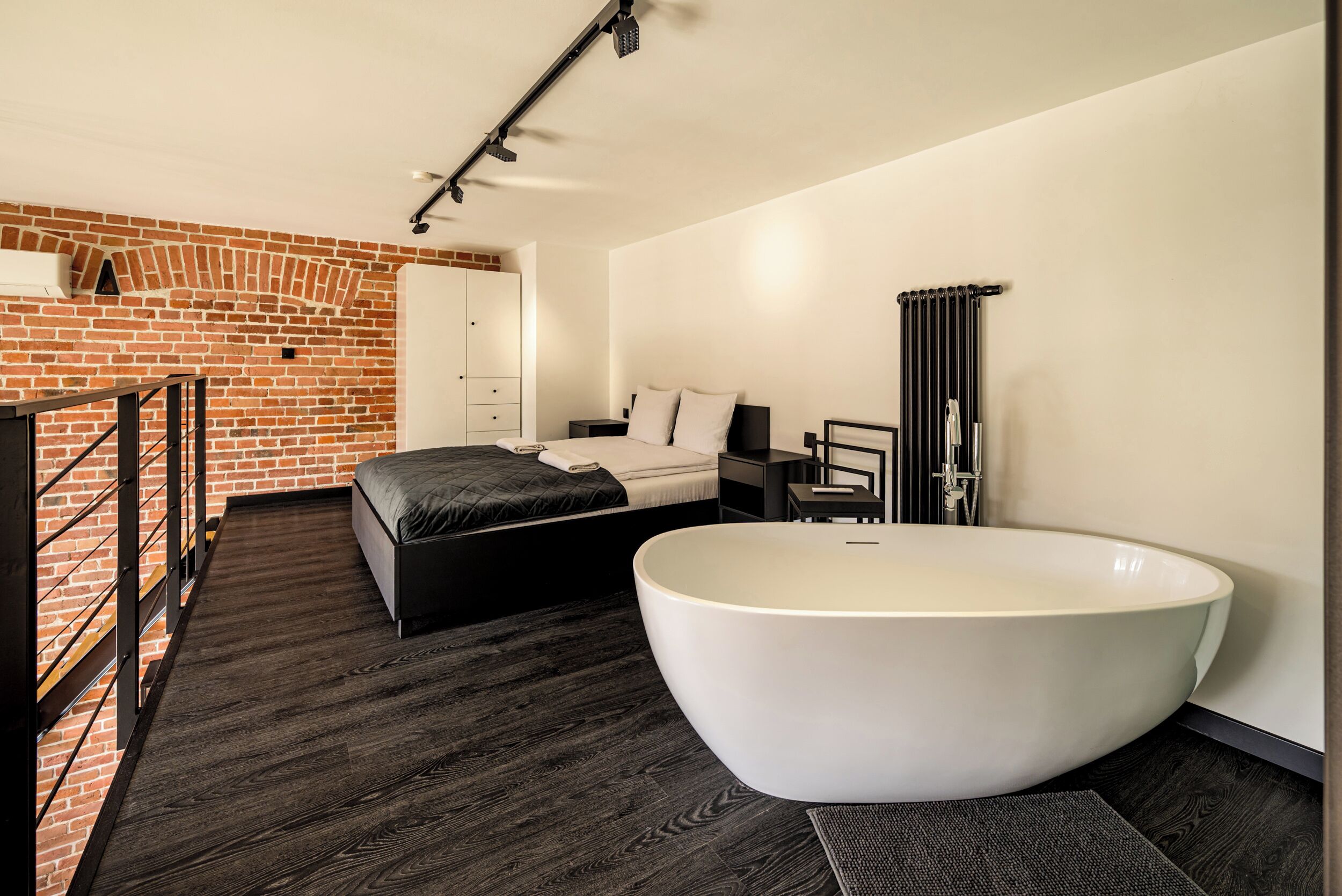 Une chambre à coucher moderne avec une grande baignoire, un mur en briques et un plancher en bois.