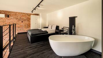 Une chambre à coucher moderne avec une grande baignoire, un mur en briques et un plancher en bois.