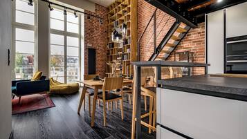 A modern kitchen with a brick wall, wooden shelving, and a dining area with a table and chairs.