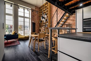 A modern kitchen with a brick wall, wooden shelving, and a dining area with a table and chairs. - RentPlanet - Bulwar Staromiejski (Wroclaw)