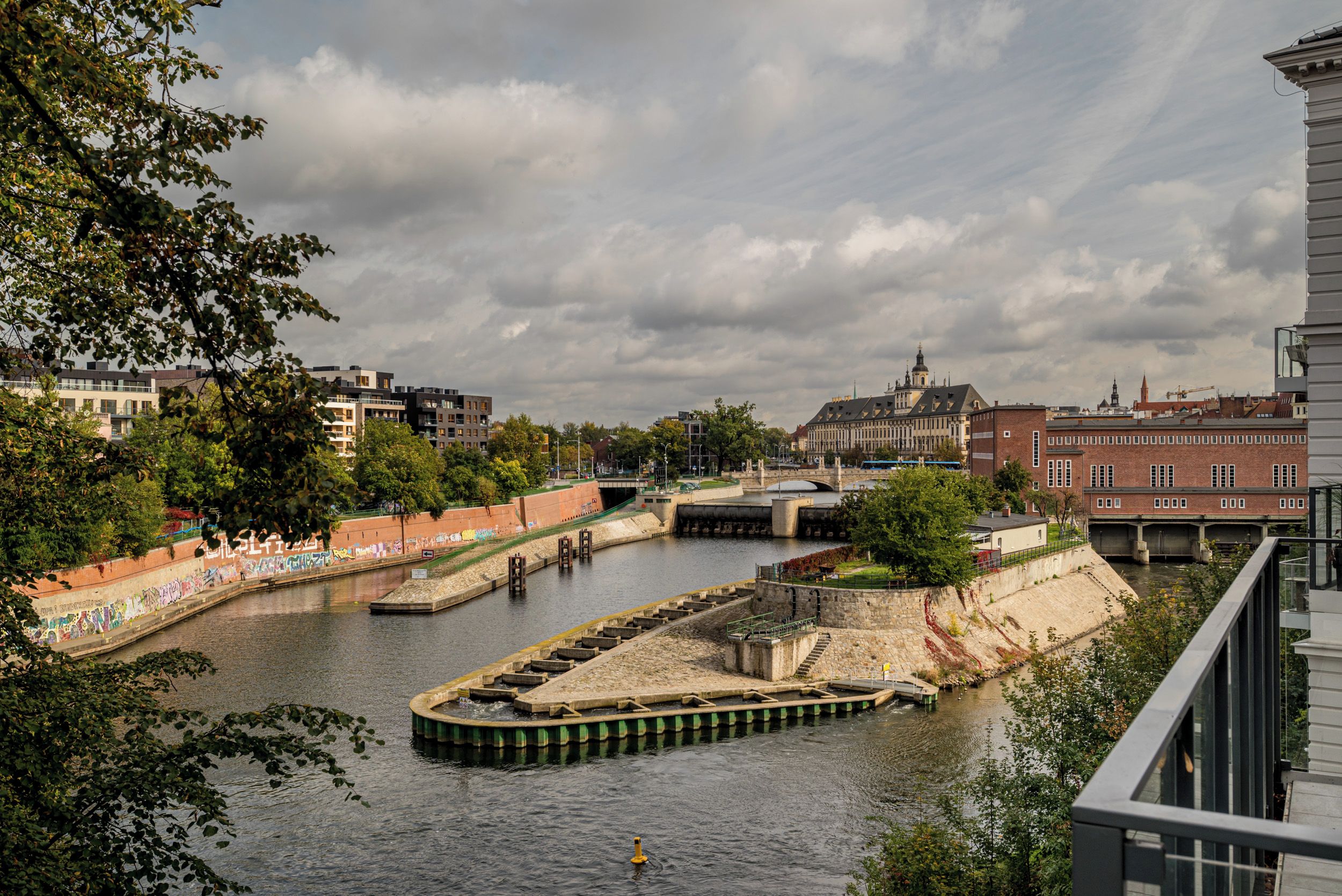 Ein Fluss mit Schleusen, umgeben von Gebäuden und Bäumen.
