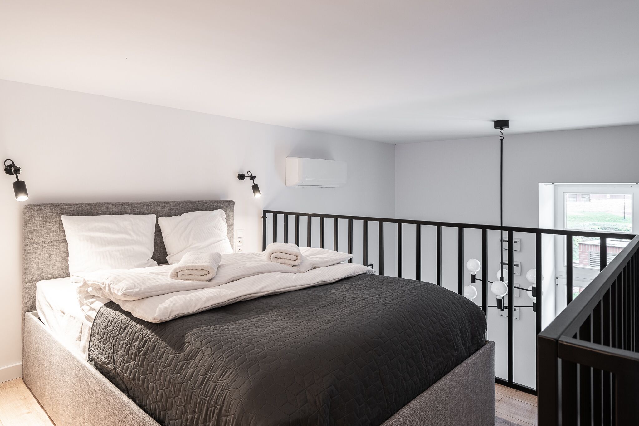 Un dormitorio moderno con una cama grande, cabecera, balcón con barandilla y ventana.