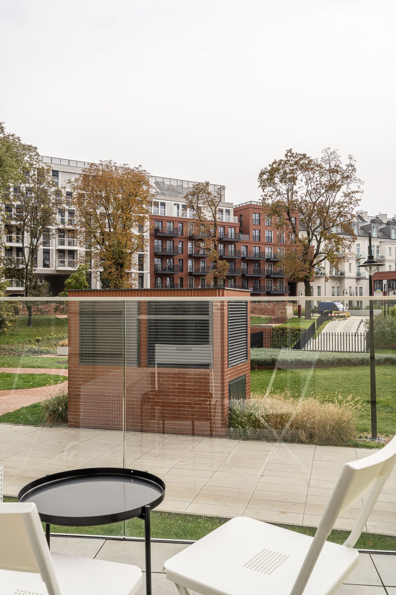 Un patio con una mesa redonda y sillas, una estructura de ladrillo y vistas a edificios residenciales al fondo.