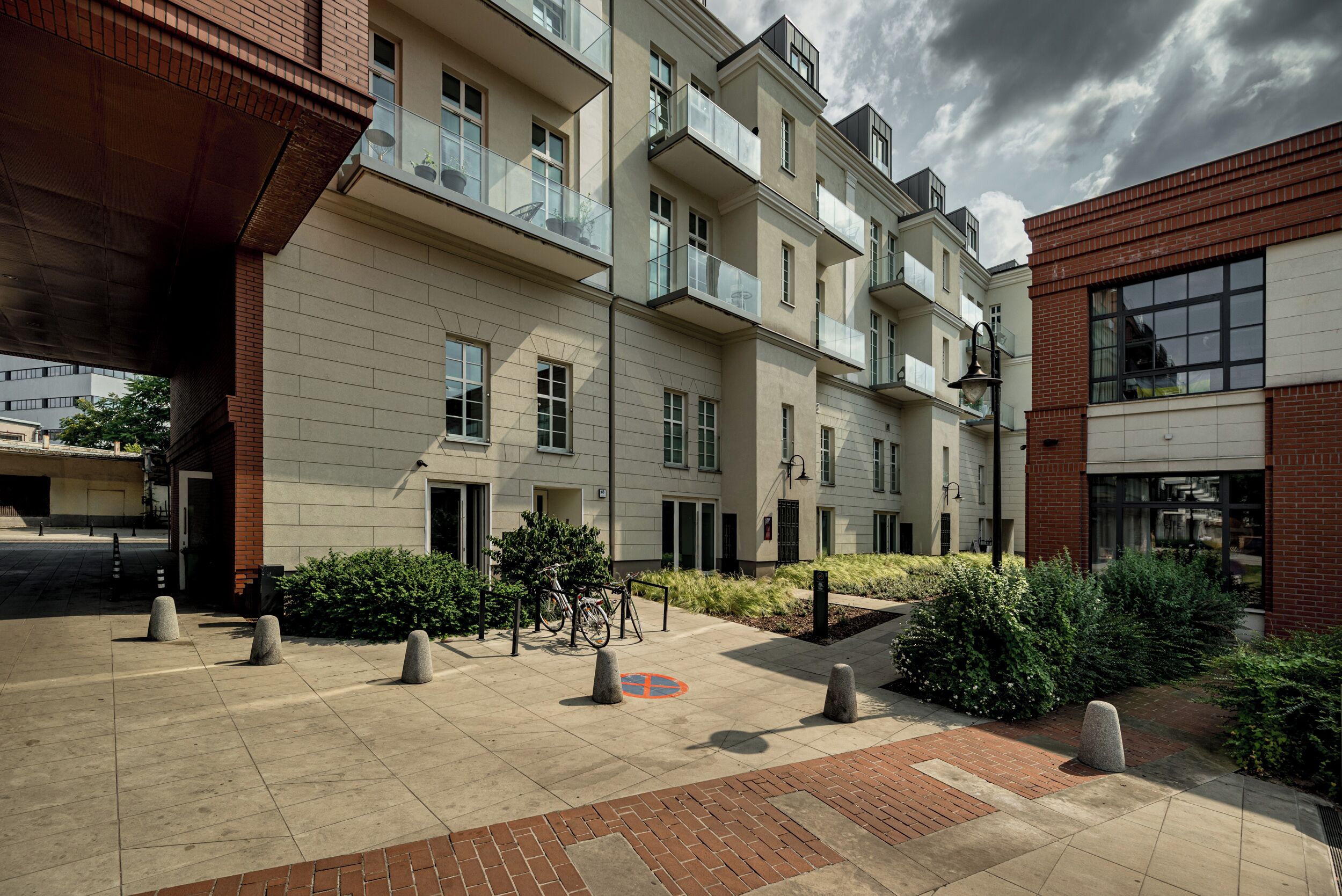 A multi-story residential building with balconies, a paved courtyard, and a brick facade.