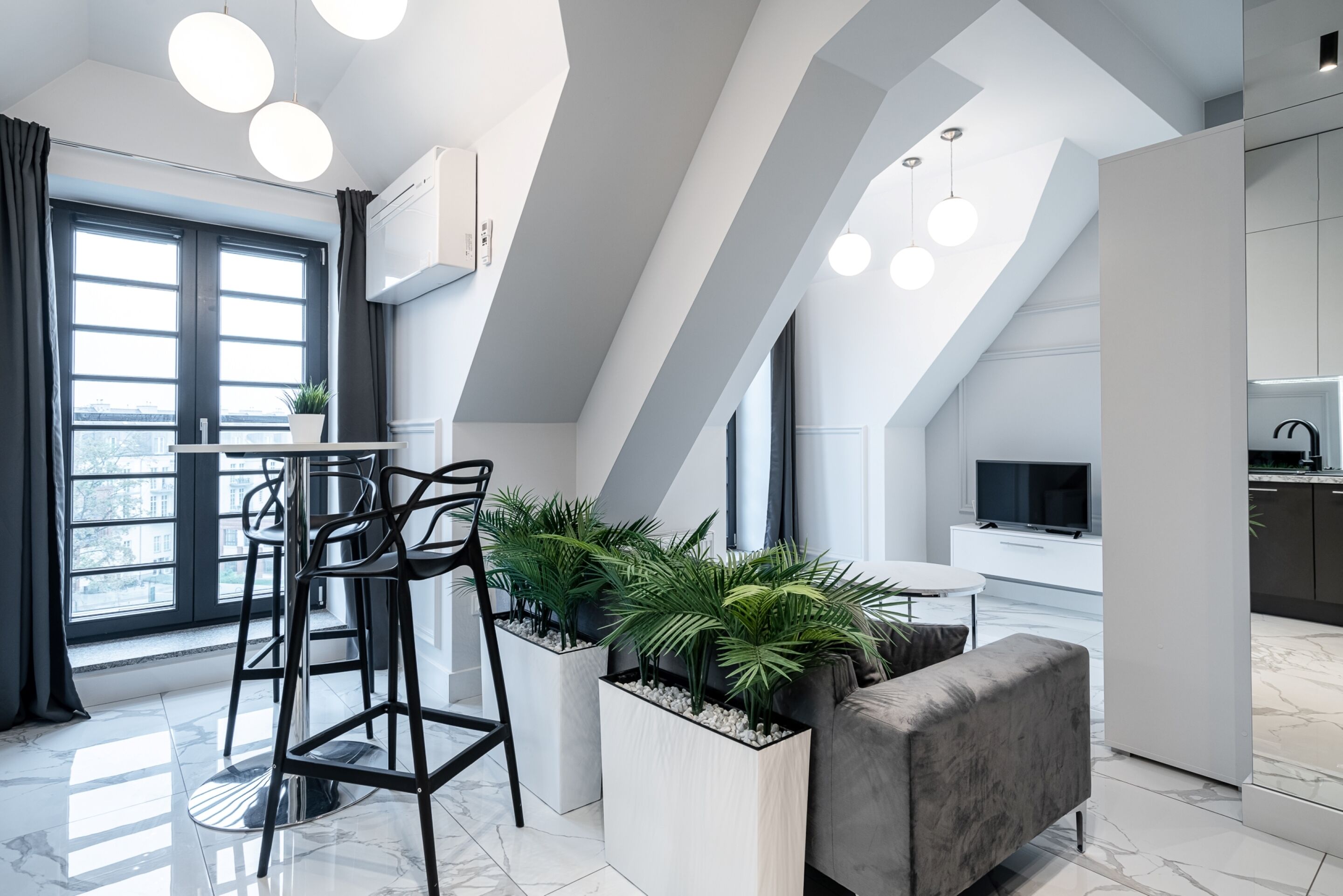 Una cocina moderna con horno empotrado, un comedor con mesa blanca y sillas negras, y un sofá gris.