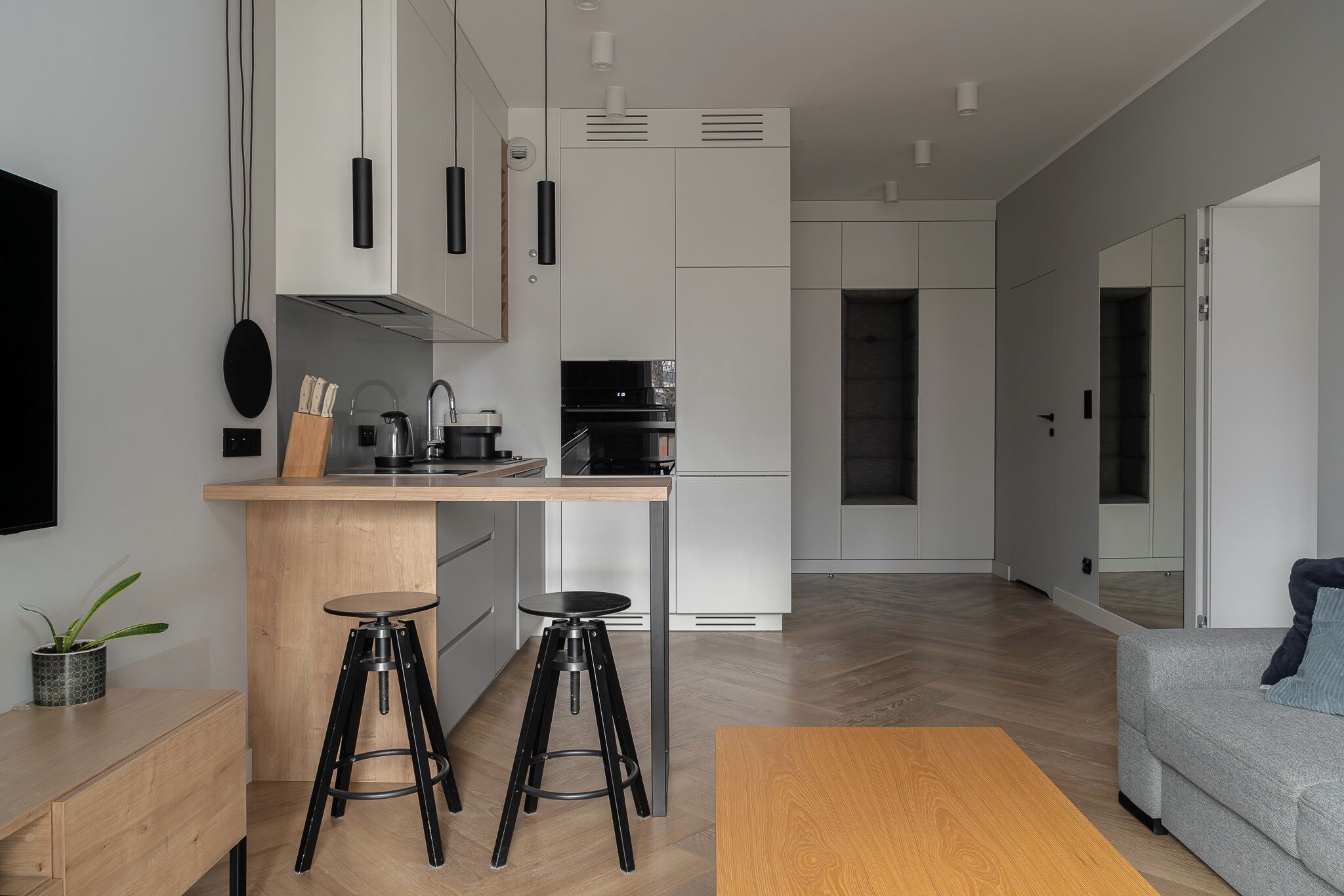 Une cuisine moderne avec des meubles blancs, un plan de travail en bois et une cuisinière noire. On y trouve deux tabourets noirs et une table en bois.