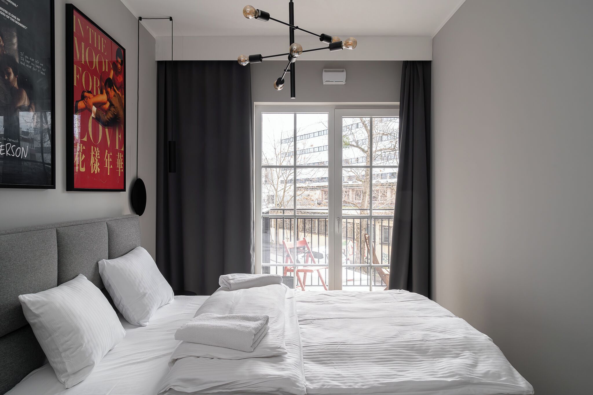 Una habitación de hotel moderna con una cama grande, cabecera gris y vistas al balcón exterior.