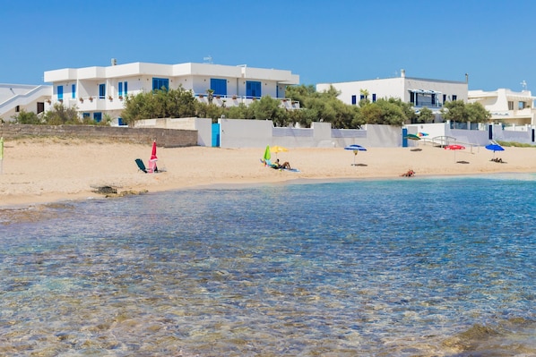 A beach with clear water, white buildings with blue accents, and people relaxing.