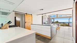 Une cuisine moderne dotée d’un grand îlot central, d’une porte en bois et offrant une vue sur l’océan.