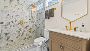 Un bagno con box doccia in vetro, un water, un lavabo con accessori dorati e un grande specchio con cornice dorata.