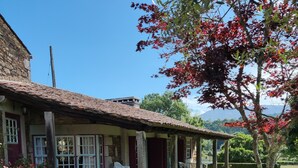 Ein rustikales Steinhaus mit Ziegeldach, einer Laube und einem kleinen Garten mit Rasenfläche und Baum.