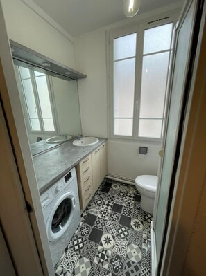 A compact bathroom with a washing machine, a sink, and a toilet.