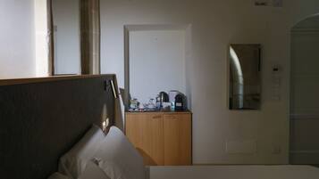 A hotel room with a bed, a wooden wardrobe, a desk with a coffee maker, and a mirror on the wall.