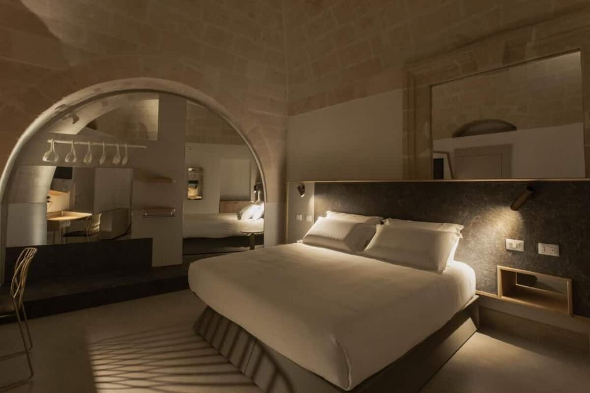 A modern hotel room with a large bed, a dining area, and a bathroom.