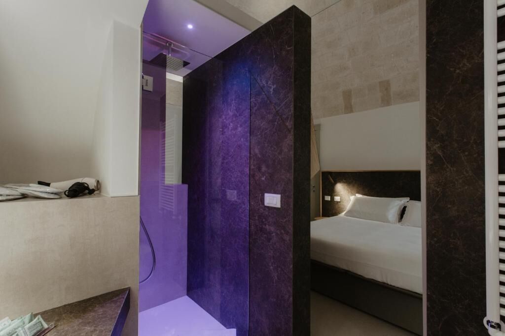 A modern hotel room with a bed, a bathroom with a shower, and a purple partition.