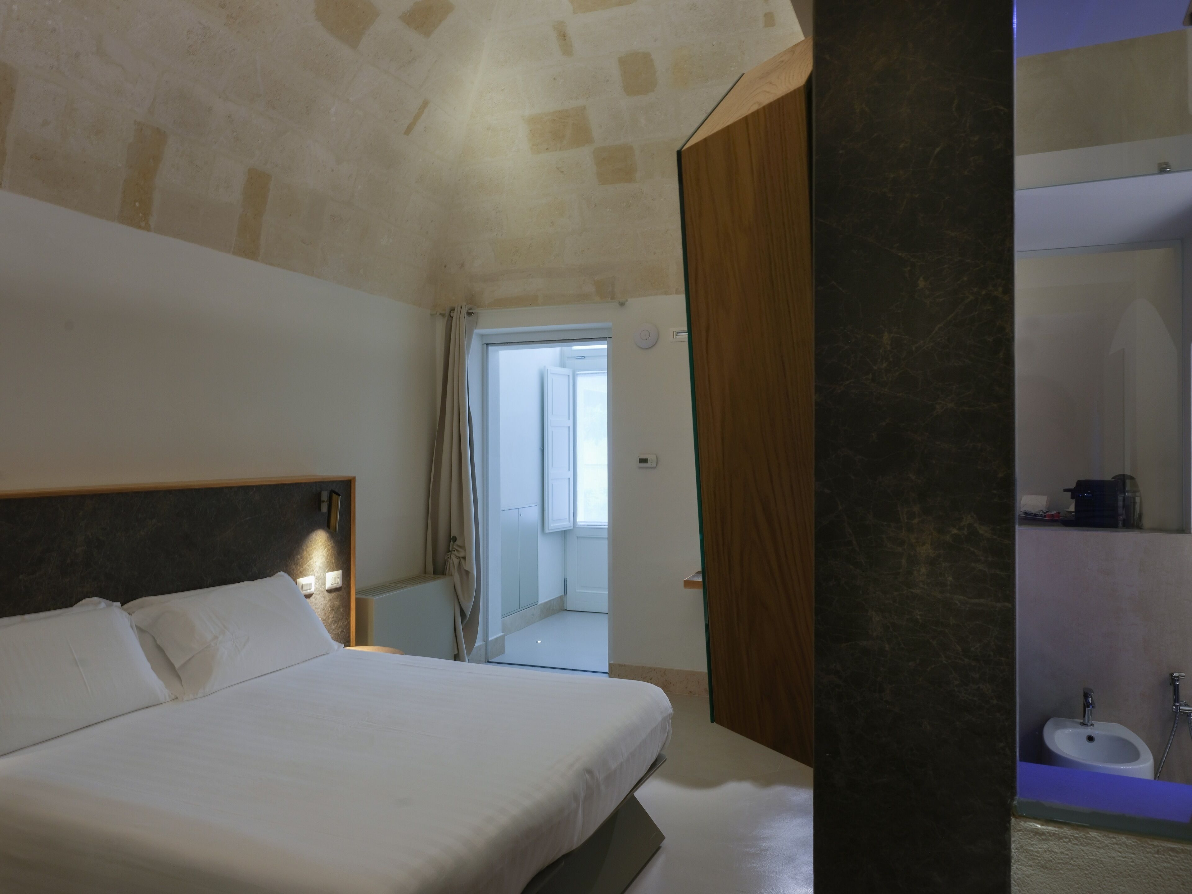 A bedroom with a bed, a wooden headboard, a bathroom with a sink and mirror, and a door leading to another room.