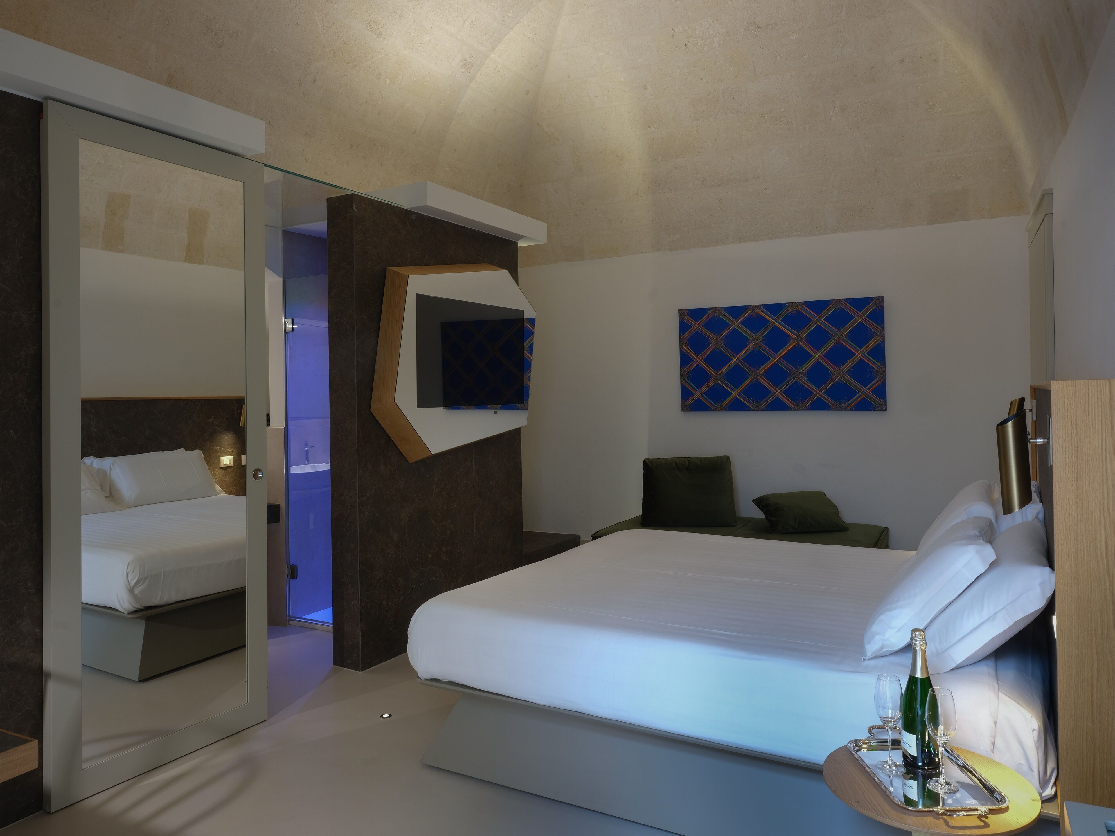 Una camera d'albergo moderna con un letto grande, una televisione a parete e un tavolino con una bottiglia e dei bicchieri.