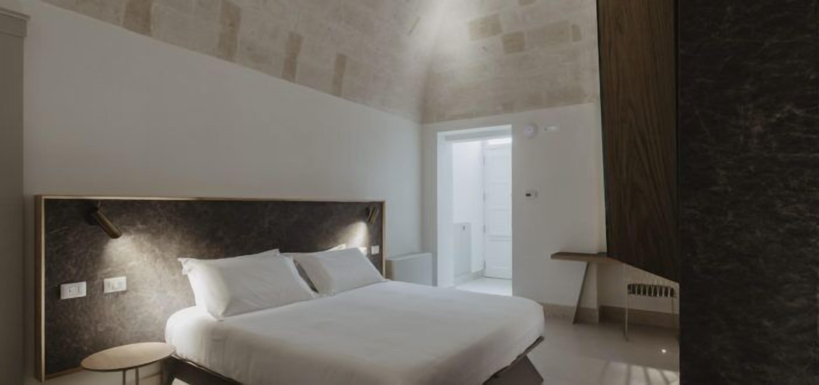 A bedroom with a large bed, a small table, and a door leading to another room.