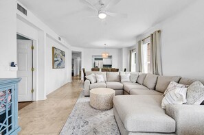 Ein großzügiges Wohnzimmer mit einer großen Eckcouch, einem runden Couchtisch und einem Deckenventilator.