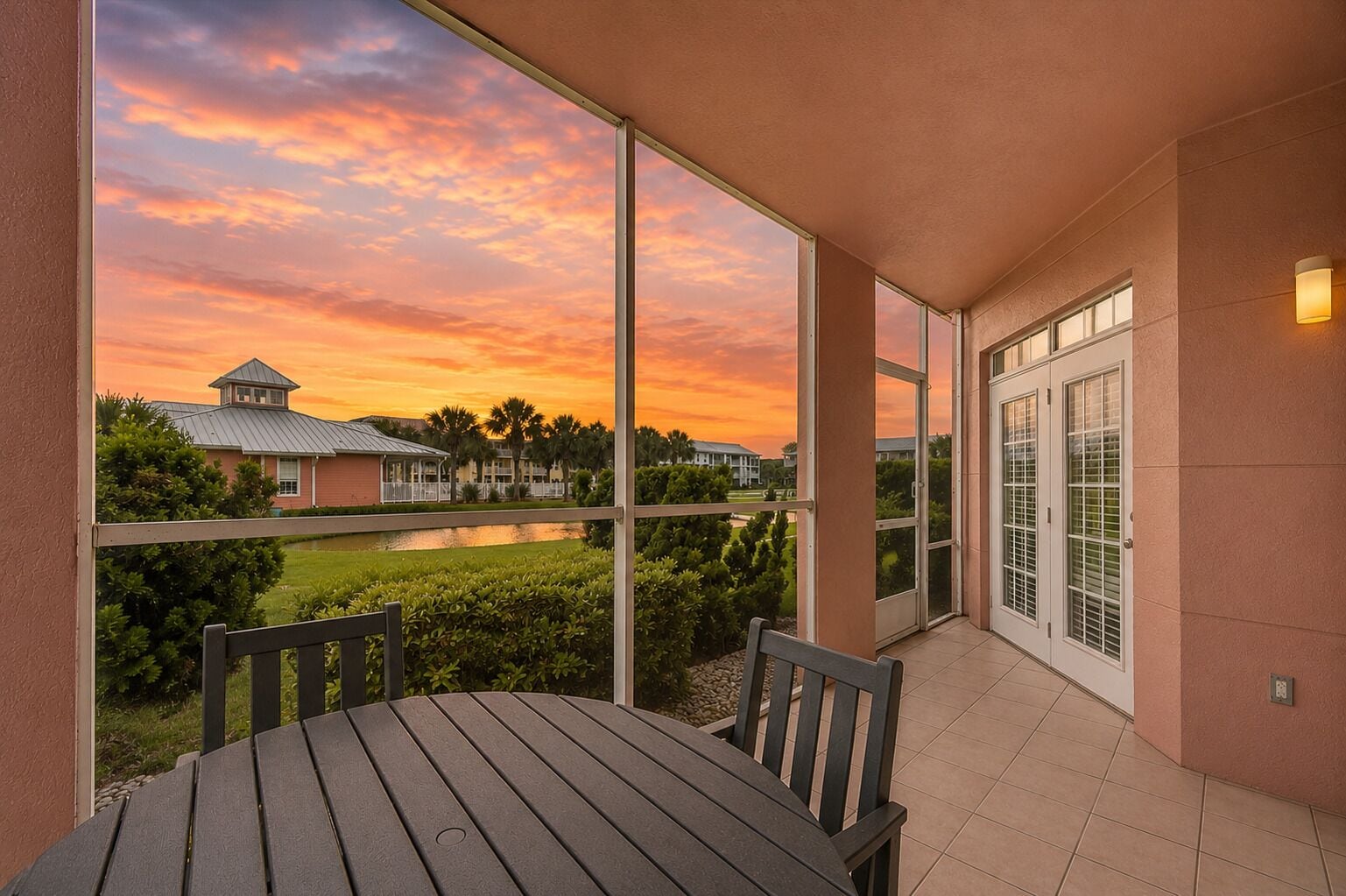 A balcony with a view of a sunset, a table, and chairs.