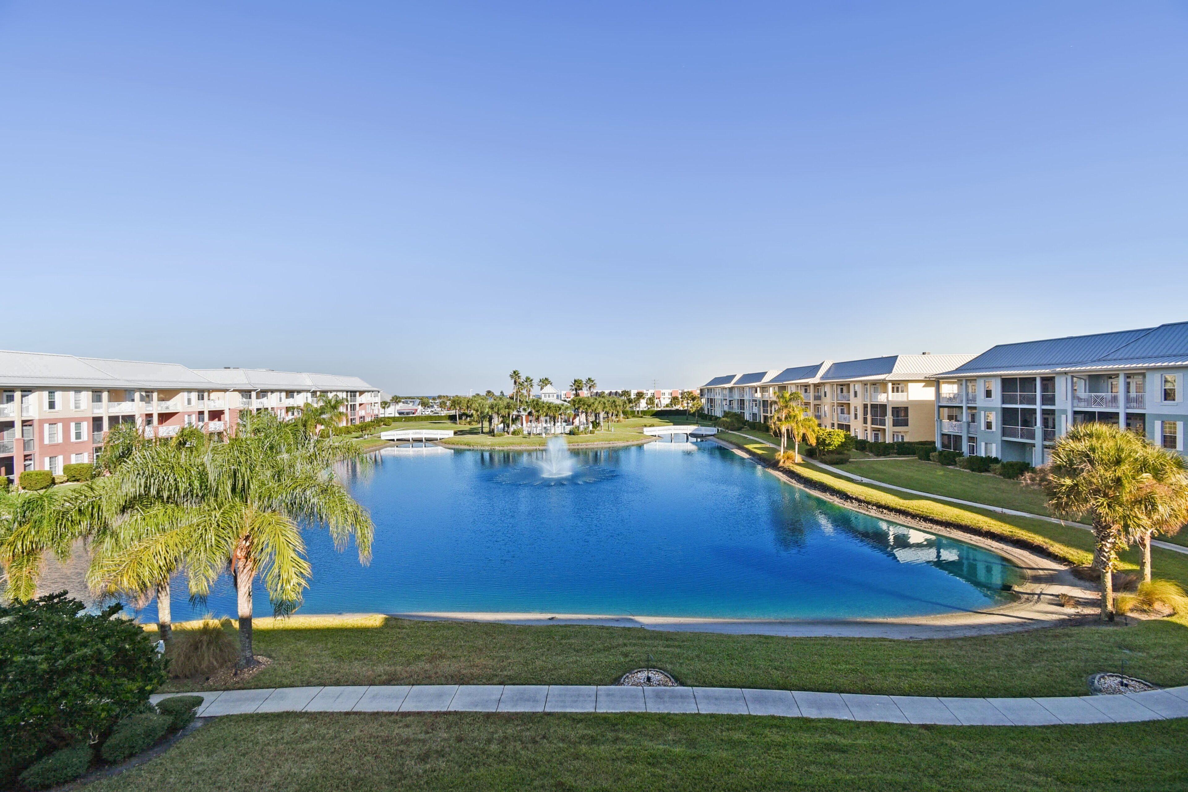 A hotel with a large swimming pool surrounded by well-maintained lawns and palm trees.