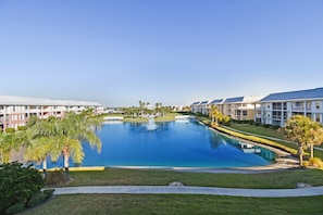 A hotel with a large swimming pool surrounded by well-maintained lawns and palm trees.