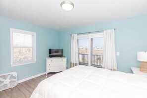A bedroom with a bed, a dresser, a television, and a balcony with curtains.
