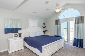 A bedroom with a bed, a nightstand, a ceiling fan, a window with curtains, and a painting on the wall.