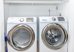 A pair of Samsung front-loading washers with control panels, a power outlet, and a vent.