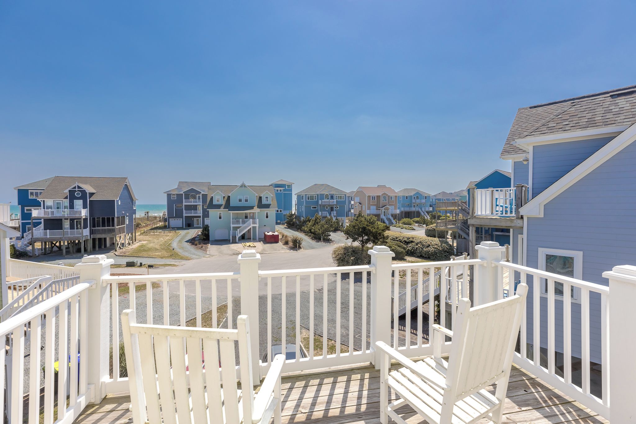 Una zona residencial costera con varias casas de dos pisos, una terraza de madera y vista despejada al océano.
