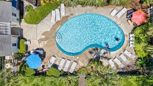 An aerial view of a swimming pool surrounded by lounge chairs and umbrellas, with a pathway leading to a building.